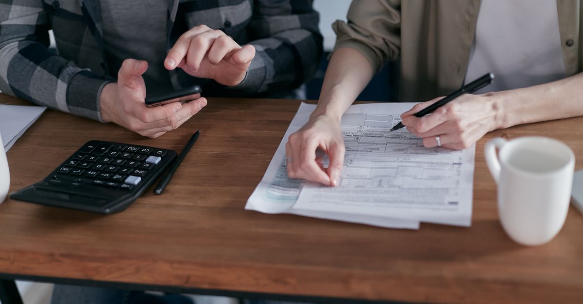 Two people reviewing tax paperwork and working out figures at a desk with a calculator