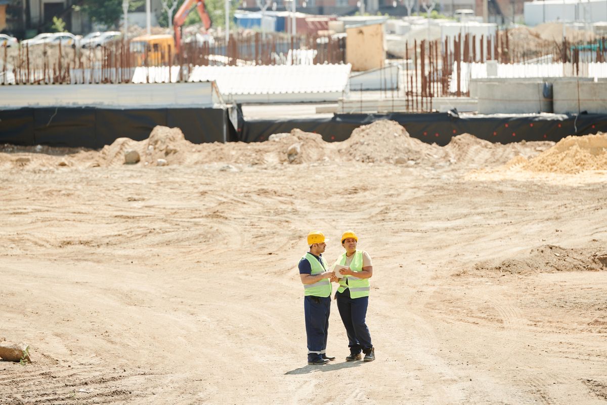 Two construction workers in safety gear discussing plans on a building site