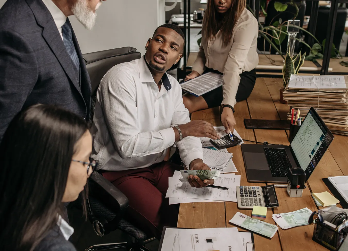 Small business colleagues counting cash and working through payroll paperwork at a desk with calculators and a laptop