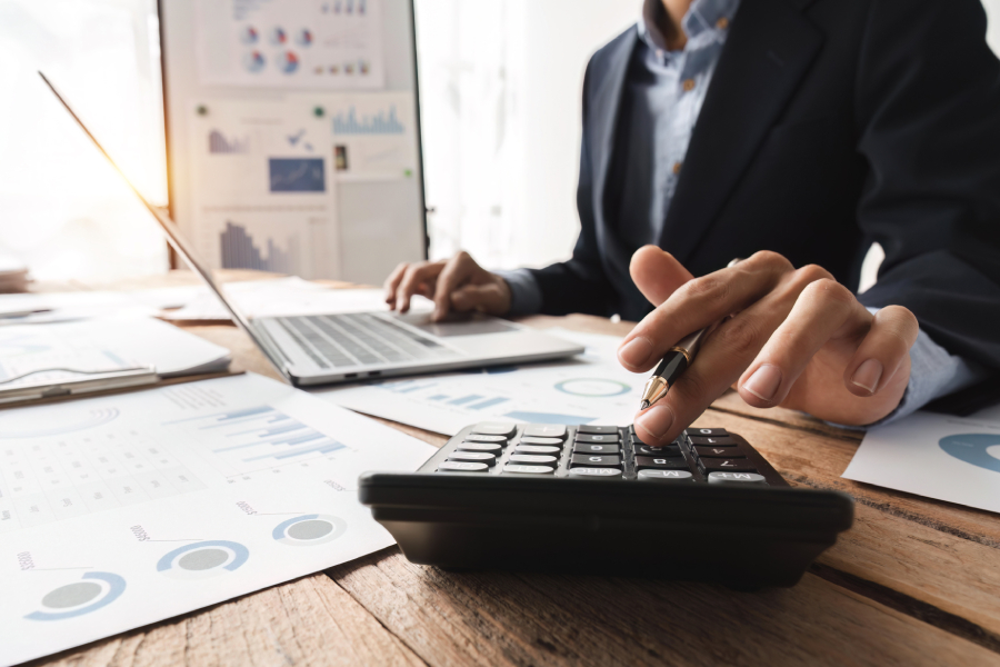 Accountant working through company accounts figures with a calculator, laptop and financial paperwork on a desk