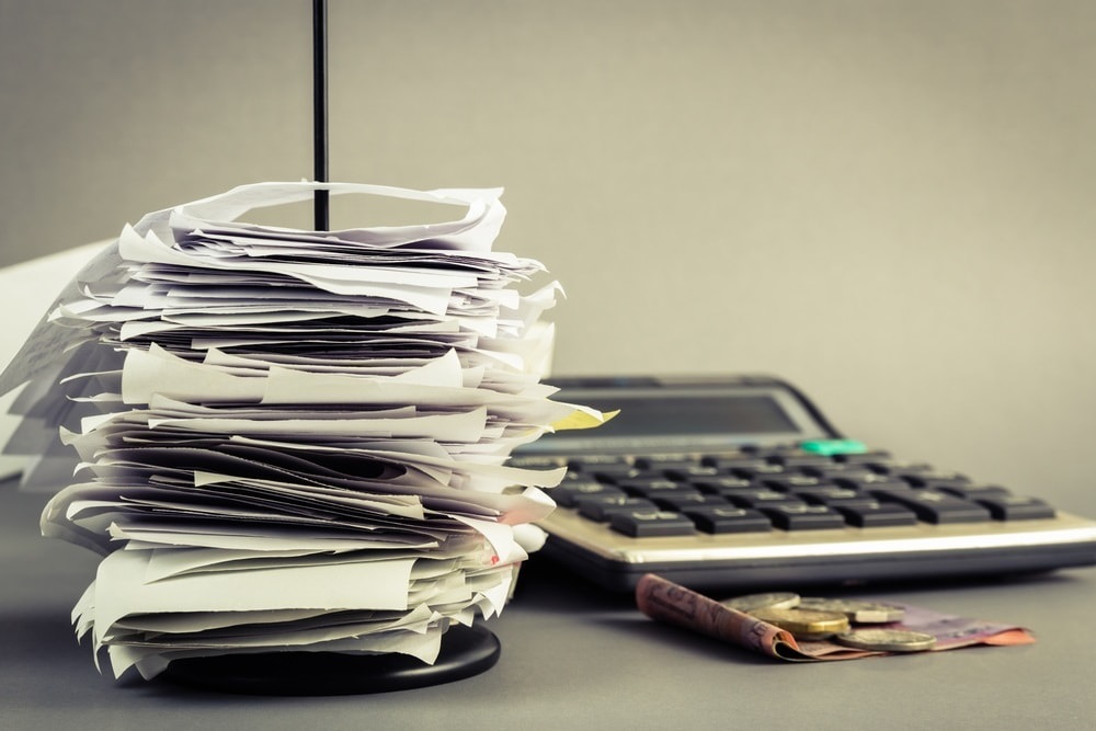 A tall stack of unsorted paper receipts next to a calculator on a desk